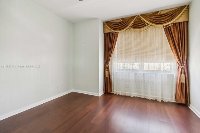 spare room featuring dark wood-style flooring and baseboards
