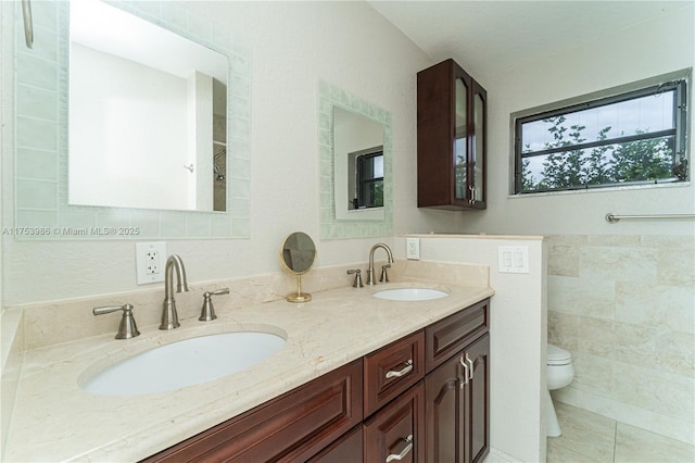 bathroom featuring toilet, double vanity, tile walls, and a sink