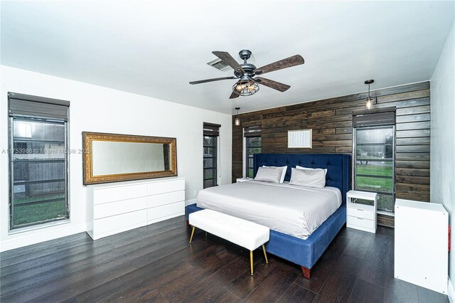 bedroom with an accent wall, a ceiling fan, wooden walls, wood finished floors, and baseboards