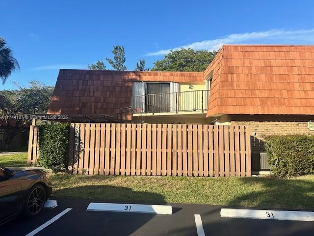 view of side of property featuring uncovered parking, fence, mansard roof, and brick siding