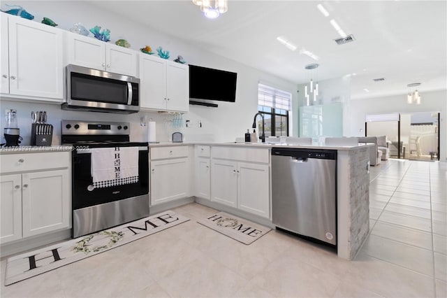 kitchen with visible vents, white cabinets, a peninsula, stainless steel appliances, and a sink