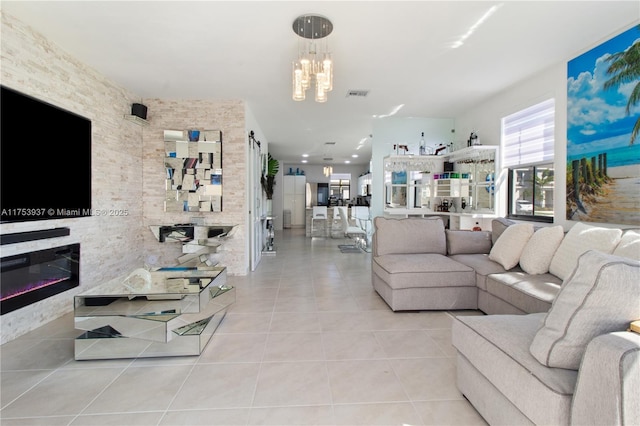 living room featuring a glass covered fireplace, visible vents, a notable chandelier, and tile patterned floors