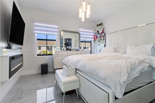 bedroom featuring light tile patterned floors, an inviting chandelier, a glass covered fireplace, and baseboards