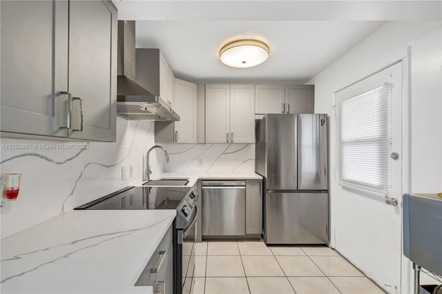 kitchen with light tile patterned floors, backsplash, appliances with stainless steel finishes, a sink, and wall chimney exhaust hood