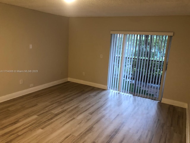 unfurnished room featuring a textured ceiling, baseboards, and wood finished floors