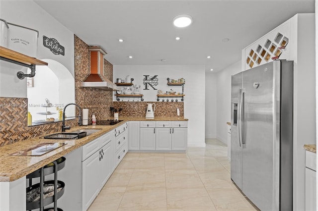 kitchen featuring stainless steel fridge, light stone counters, open shelves, and a sink