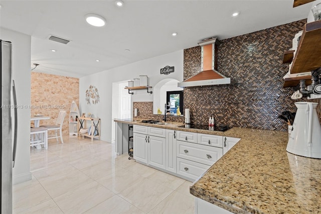 kitchen with black electric cooktop, a sink, white cabinetry, wall chimney range hood, and tasteful backsplash