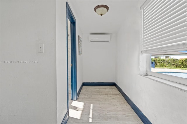 hallway with light wood-style floors, baseboards, and a wall mounted AC