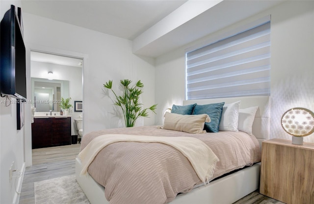 bedroom with ensuite bathroom and light wood finished floors