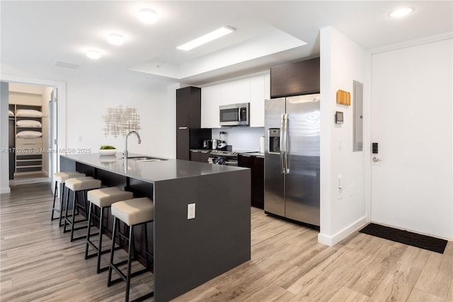 kitchen featuring light wood-style flooring, modern cabinets, stainless steel appliances, a kitchen bar, and a sink