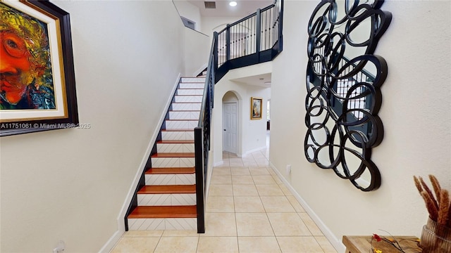 stairway featuring arched walkways, tile patterned flooring, a high ceiling, visible vents, and baseboards