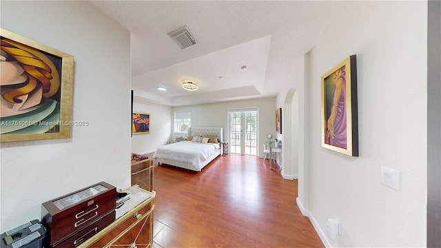 bedroom featuring baseboards, arched walkways, visible vents, a raised ceiling, and wood finished floors