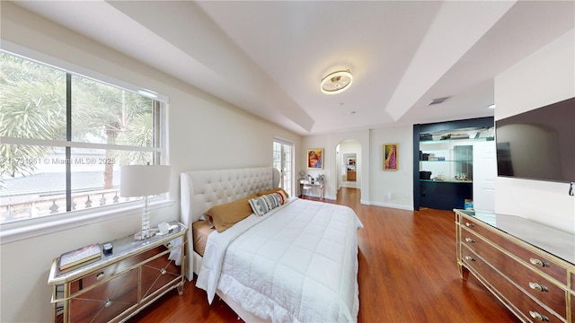 bedroom with arched walkways, baseboards, dark wood finished floors, and a tray ceiling