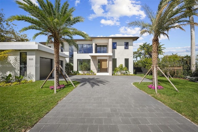 contemporary home with a front lawn, decorative driveway, an attached garage, and stucco siding