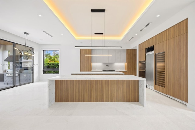 kitchen with brown cabinetry, a large island, modern cabinets, a tray ceiling, and pendant lighting