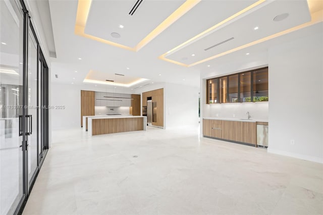 unfurnished living room with a tray ceiling, marble finish floor, visible vents, and baseboards