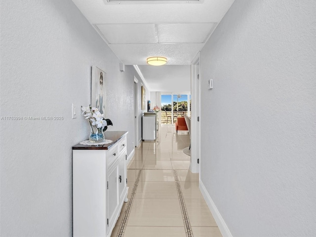 hallway with light tile patterned floors, baseboards, and a textured wall