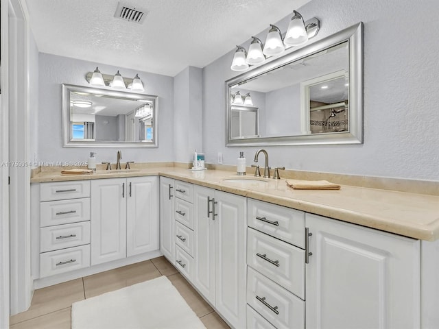 bathroom with a textured ceiling, double vanity, a sink, and visible vents