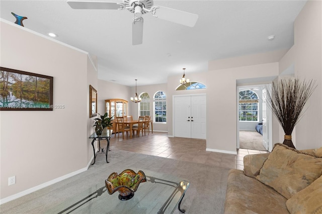 carpeted living room featuring ceiling fan with notable chandelier, baseboards, and tile patterned floors