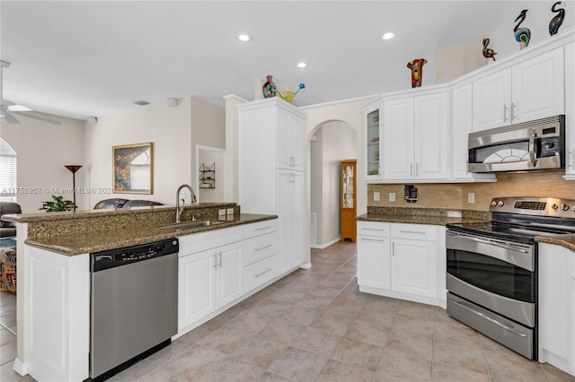 kitchen with appliances with stainless steel finishes, arched walkways, dark stone counters, and a sink