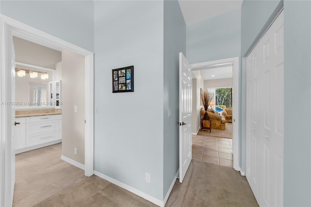 corridor with baseboards and light colored carpet