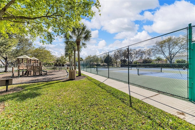 view of tennis court with playground community, a lawn, and fence