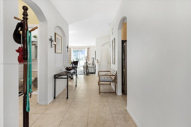 hallway with light tile patterned floors, baseboards, arched walkways, and a textured ceiling