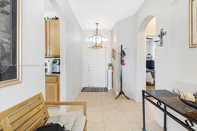 foyer featuring arched walkways, light tile patterned flooring, a notable chandelier, and baseboards