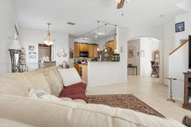 living area with arched walkways, light tile patterned floors, a textured ceiling, and visible vents