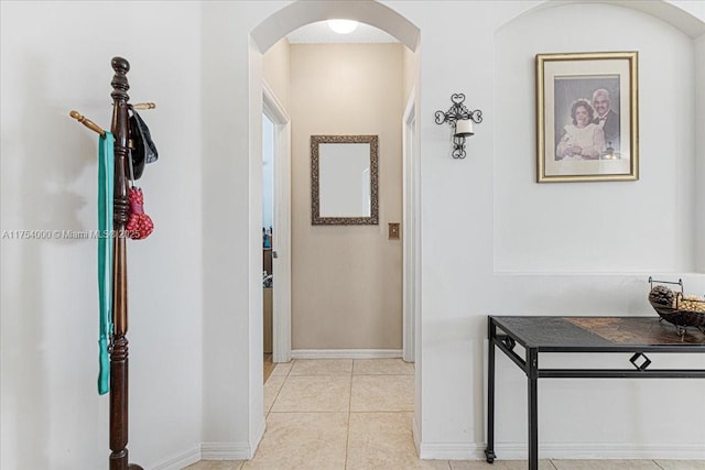 hallway with light tile patterned floors, baseboards, and arched walkways