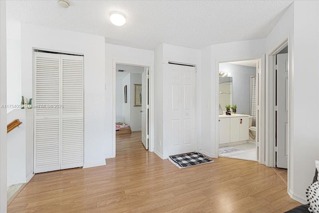 hallway featuring a textured ceiling, light wood-type flooring, and baseboards