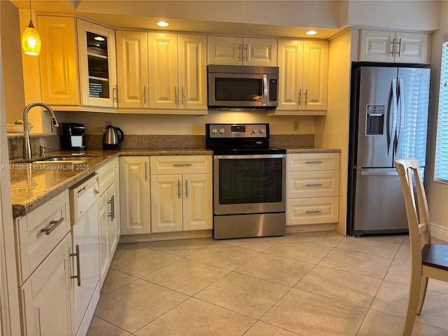 kitchen featuring light tile patterned floors, stainless steel appliances, a sink, dark stone countertops, and glass insert cabinets