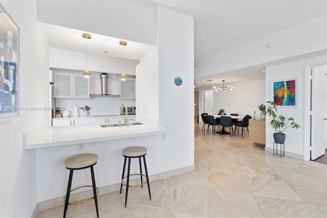 kitchen with a breakfast bar, decorative light fixtures, light countertops, glass insert cabinets, and wall chimney exhaust hood