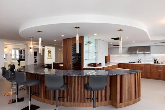 kitchen with a large island, a breakfast bar area, backsplash, ventilation hood, and modern cabinets