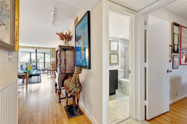 hall with rail lighting, a textured ceiling, baseboards, and wood finished floors