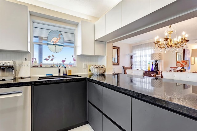 kitchen with decorative light fixtures, stainless steel dishwasher, white cabinetry, a sink, and dark stone counters