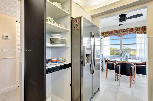 kitchen with light tile patterned floors, stainless steel fridge with ice dispenser, a wainscoted wall, ceiling fan, and open shelves