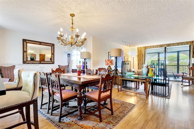 dining room with a textured ceiling, a chandelier, rail lighting, and light wood-style floors