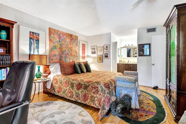 bedroom featuring ensuite bath, a textured ceiling, visible vents, and wood finished floors