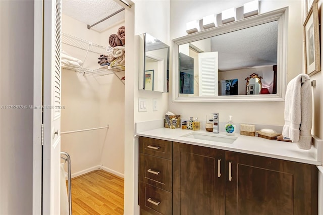 bathroom with a spacious closet, a textured ceiling, vanity, and wood finished floors