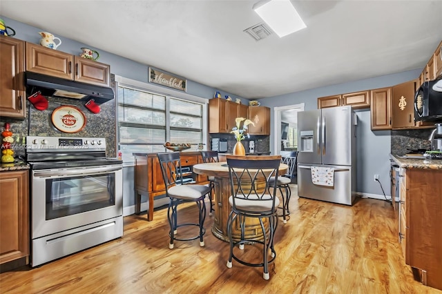 kitchen featuring under cabinet range hood, light wood-style floors, stainless steel appliances, and decorative backsplash