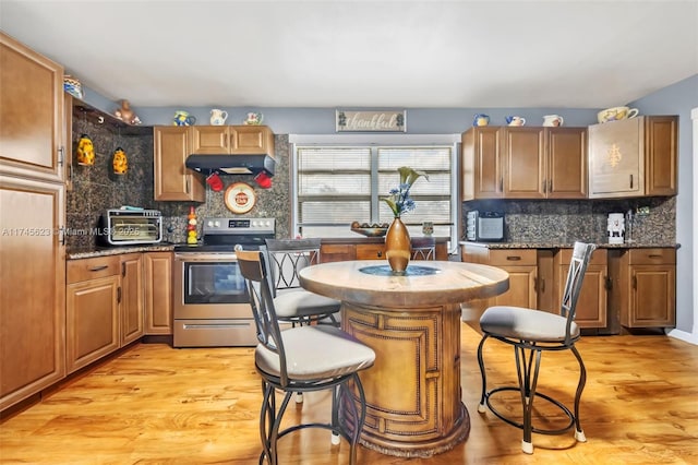 kitchen with electric range, a breakfast bar, light wood-type flooring, under cabinet range hood, and backsplash