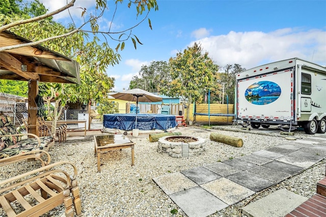 view of patio / terrace with an outdoor fire pit, a trampoline, fence, and a fenced in pool