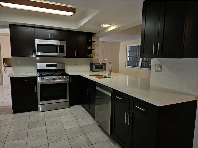 kitchen featuring stainless steel appliances, a sink, dark cabinets, and open shelves