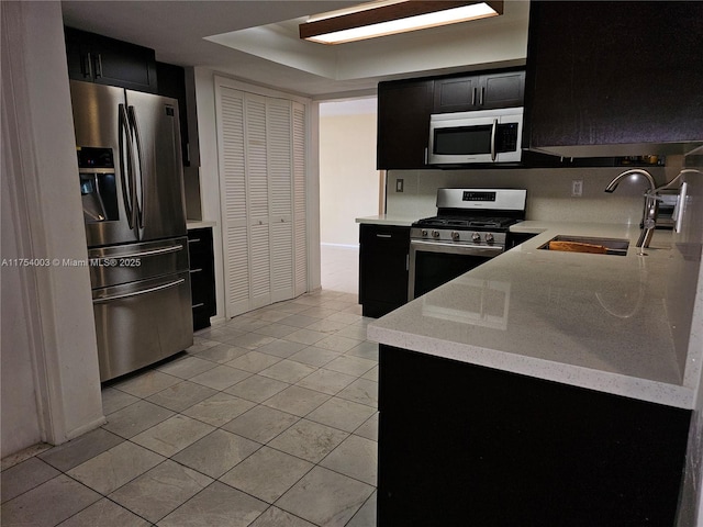 kitchen featuring light tile patterned floors, dark cabinetry, stainless steel appliances, and a sink