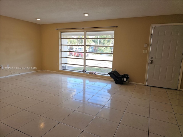 spare room with a textured ceiling, recessed lighting, light tile patterned flooring, and baseboards