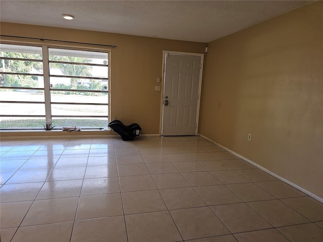 unfurnished room featuring light tile patterned floors, a textured ceiling, and baseboards