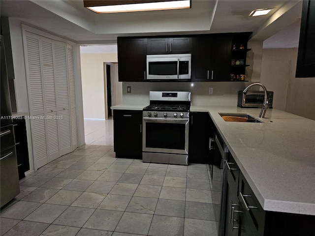 kitchen with a sink, appliances with stainless steel finishes, light countertops, and dark cabinetry