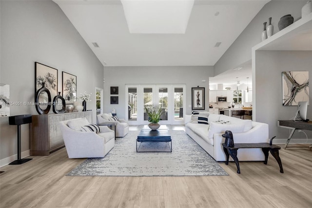 living area with light wood-style floors, visible vents, high vaulted ceiling, and baseboards