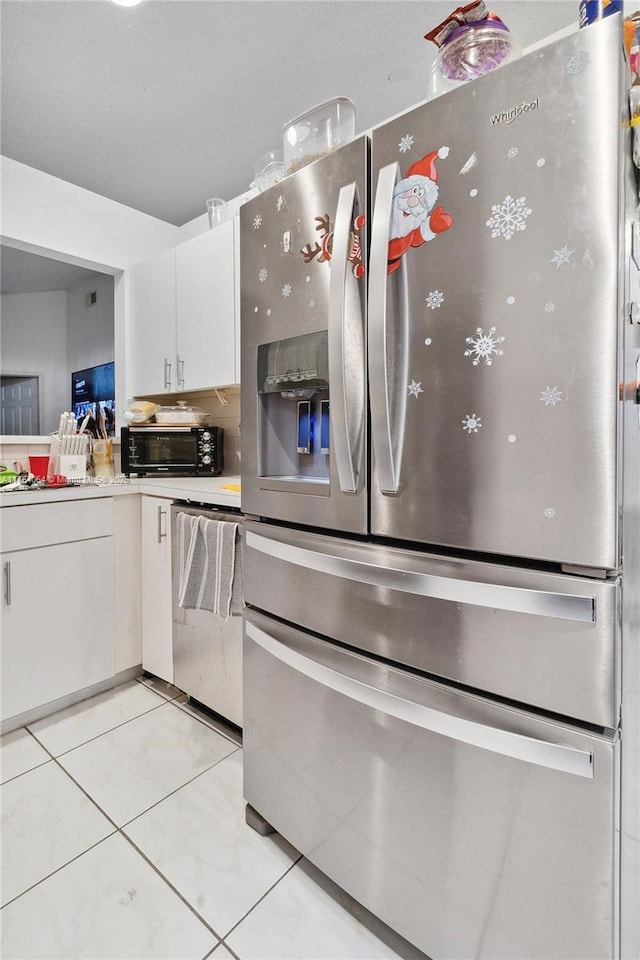 kitchen with light tile patterned floors, a toaster, stainless steel appliances, light countertops, and white cabinetry